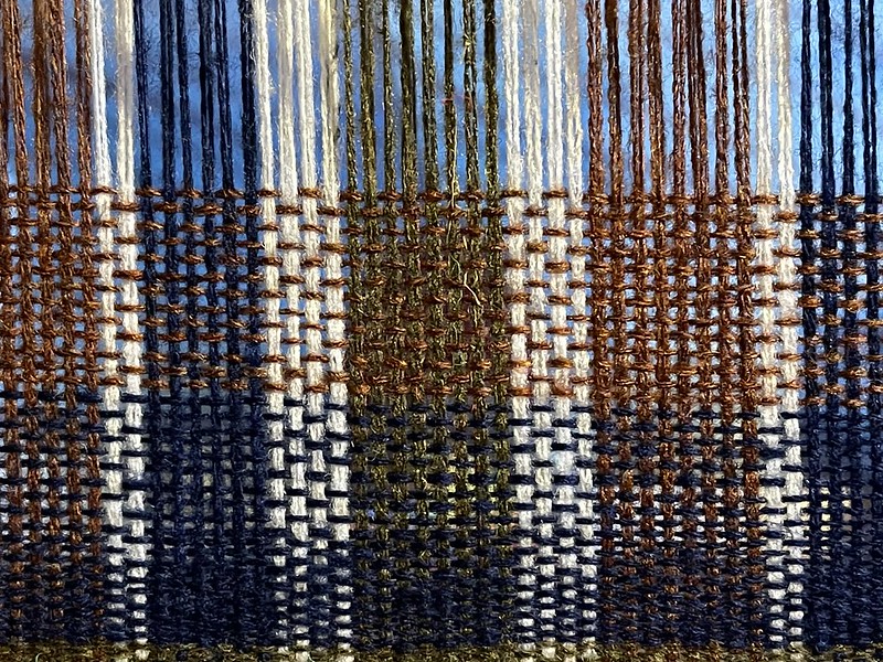 a close-up view of dark red, white, blue, and green plaid simple weaving in progress