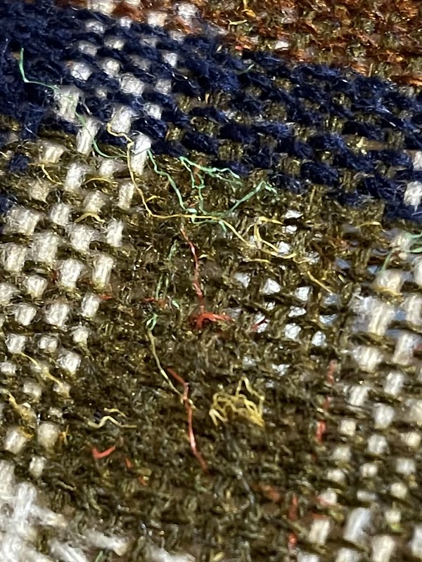 a close-up view of a green rectangle with red and yellow tweedy fibers, part of dark red, white, blue, and green plaid simple weaving in progress