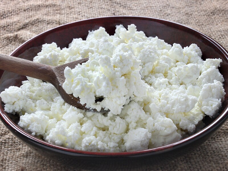 A brown bowl filled with white cottage cheese. There is a wooden spoon inside the cheese.