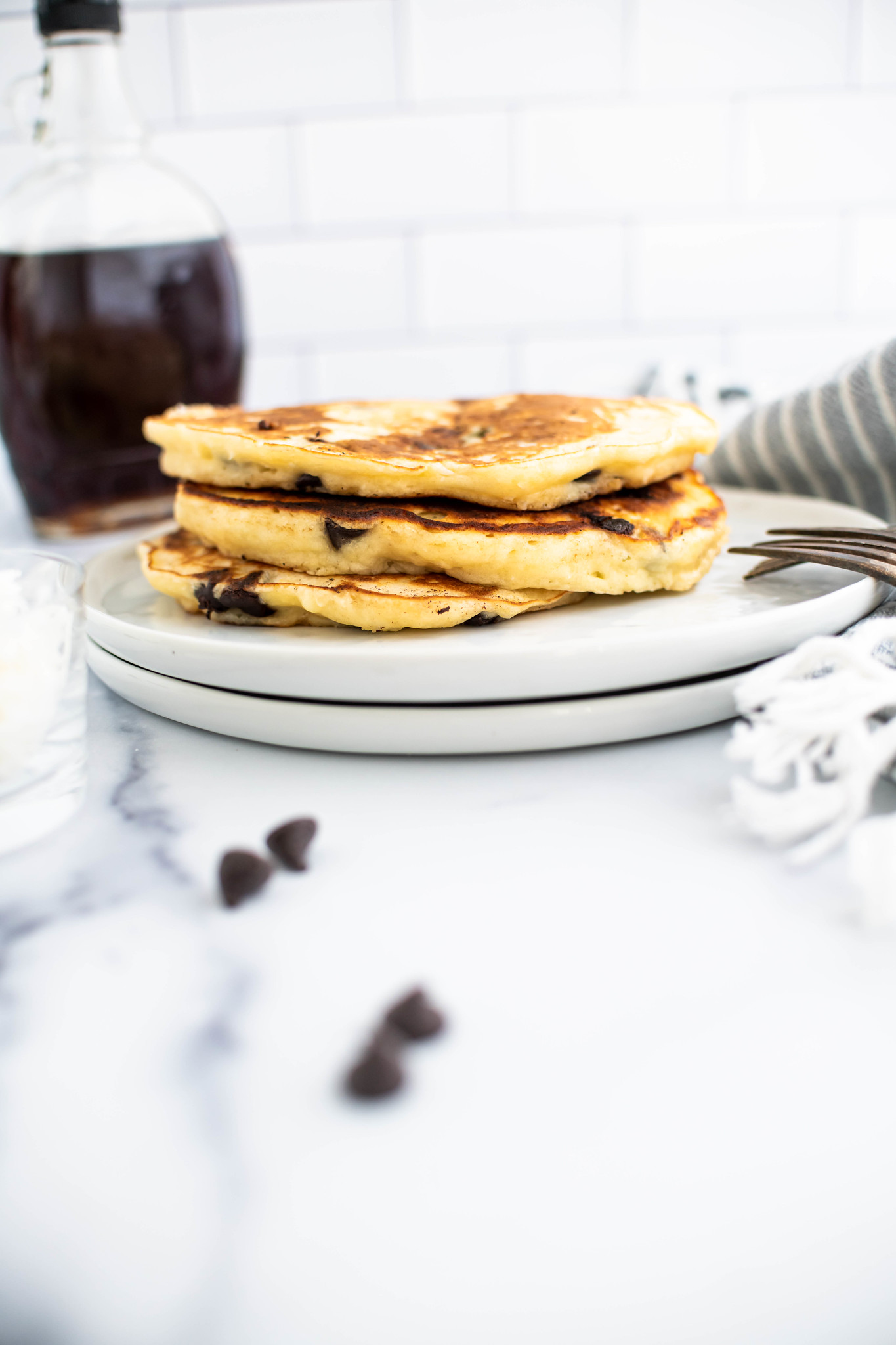 Stack of three coconut chocolate chip pancakes on a white round plate.