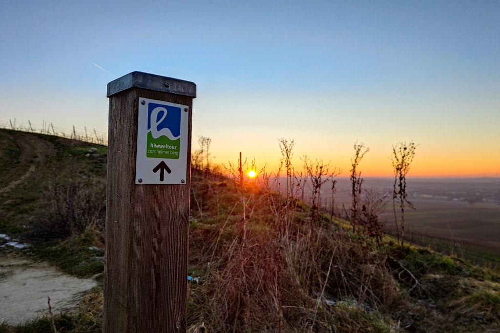 Wegezeichen Hiwweltour Zornheimer Berg mit Sonnenaufgang am Horizont