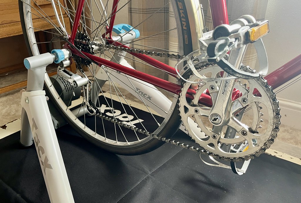 A photo of the rear wheel of a red bike clamped into the white and blue Tacx Flow smart trainer