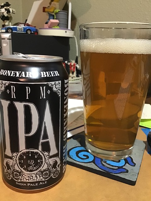 Boneyard RPM IPA can next to glass of the same on a messy desk.
