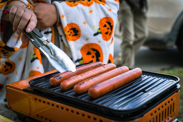 Woman cooks hot dogs on an outdoor camp grill, focus on her hand