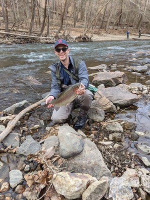 Photo of man at a creek holding a rainbow trout