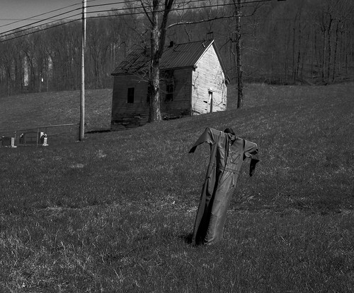 Scarecrow and the schoolhouse A scarecrow in last year&#039;s garden, an old schoolhouse, and part of a cemetery in Gifford, Magoffin County. March 1997.