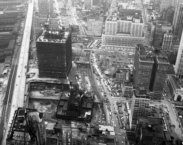 A rare aerial view of the World Trade Center's construction zone. The North Tower is about 12 floors tall while the South Tower has just begun. Abandoned 19th century piers line the Hudson. New York. 1969.