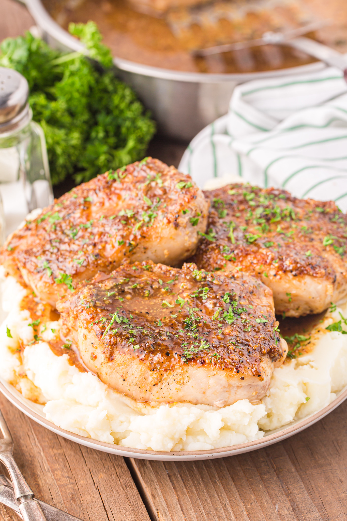 3 thick cut pork chops on top with mashed potatoes with a honey mustard sauce and fresh parsley on top