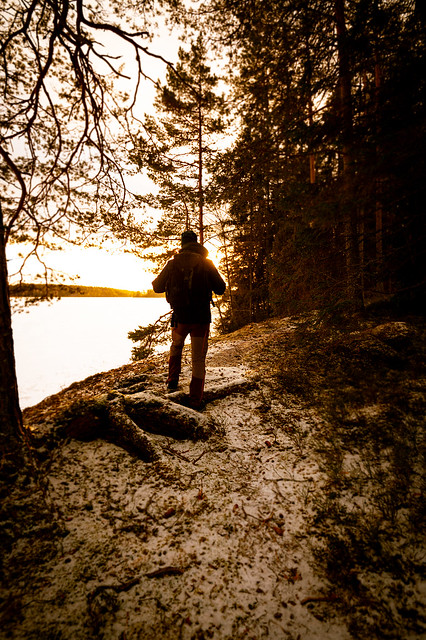 Man hiking in forest by frozen lake during sunrise in winter Sweden