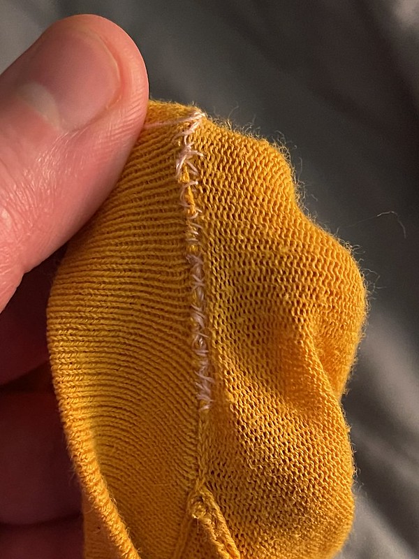inside of a yellow sweater neck mended with light pink thread in a messy whip stitch