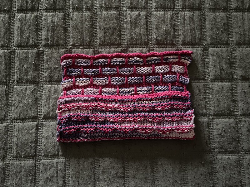 a partially folded over ballband dishcloth displaying both the front and the back of the cloth - the front looks like a brick wall with hot pink "mortar" and variegated purple "bricks", while the back has hot pink raised ridges and variegated purple "valleys"