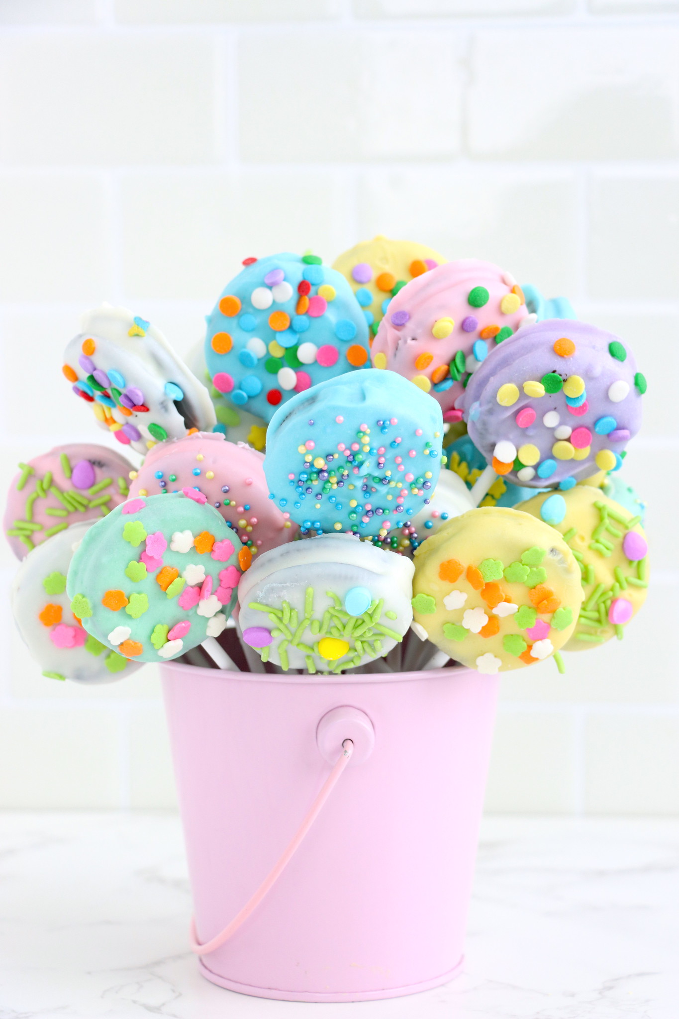Oreos coated in different colors of white chocolate and sprinkles. Shaped like a bouquet in a pastel purple bucket. 