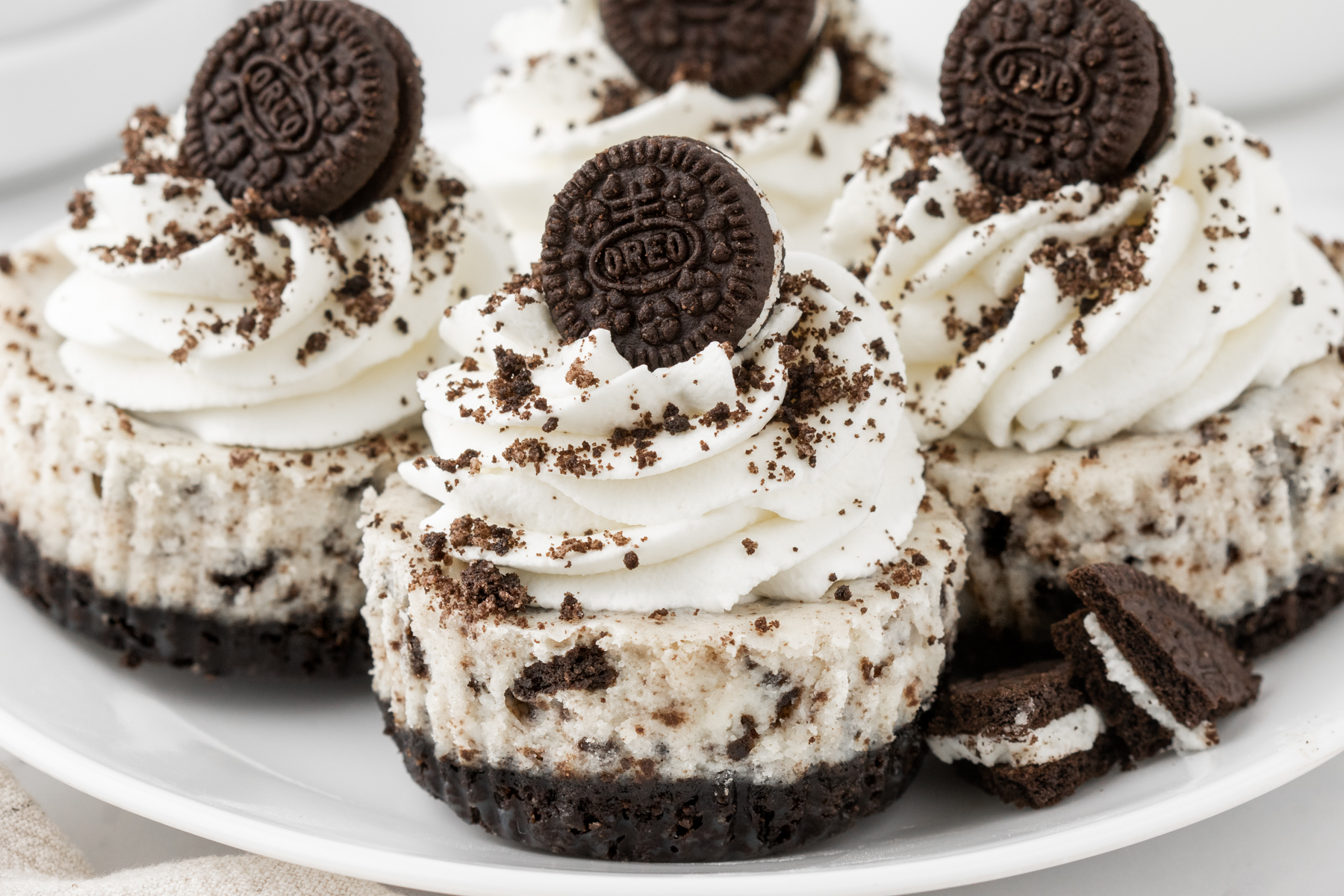 4 Oreo cheesecakes on a plate, topped with whipped cream, Oreo crumbs, and mini Oreos