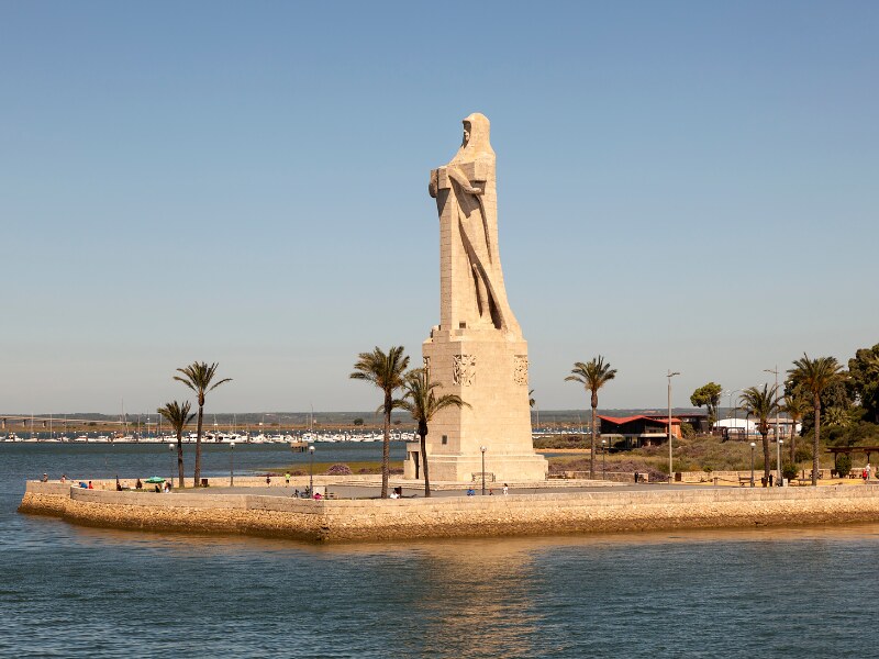 A giant statue of a man holding a cross, facing the sea