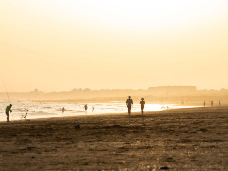 The beach at sunset. You can see the silhouettes of people walking on the sand or fishing