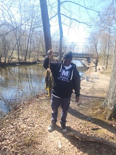 Photo of man at the side of a creek holding a large fish on a line