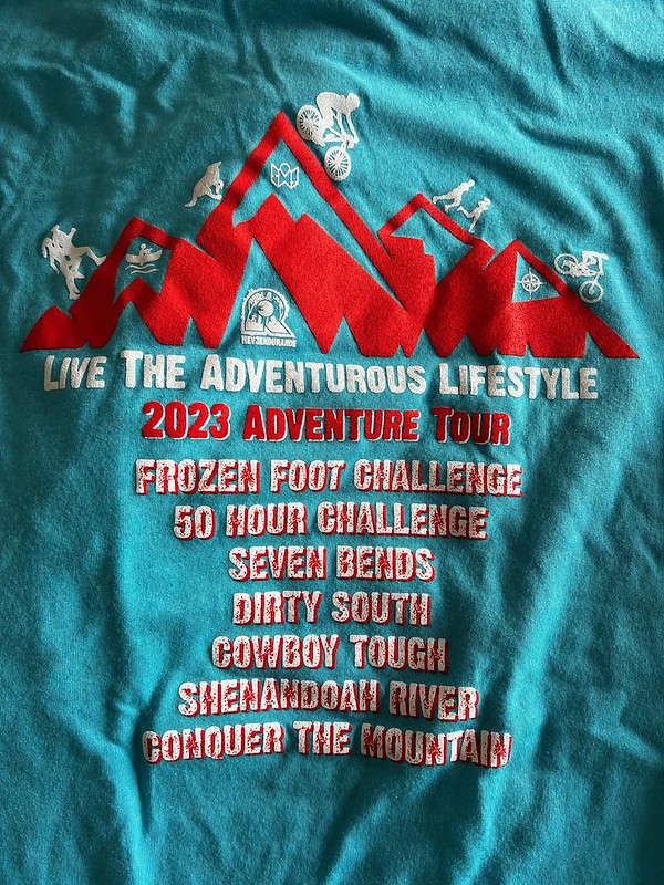 Teal blue race T-shirt with red and white lettering listing seven events.