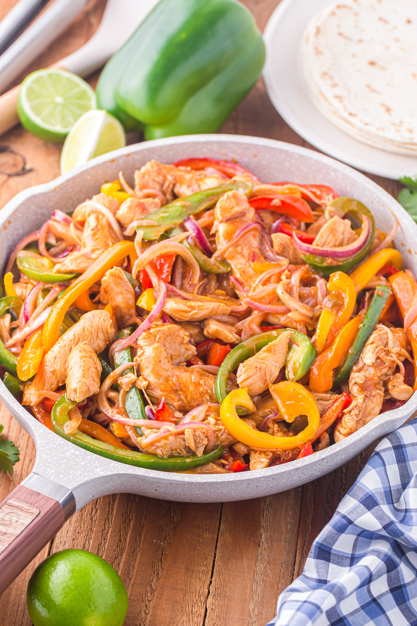 Skillet filled with chicken fajitas. Strips of chicken, sliced bell peppers, and onions coated in fajita seasoning and lime juice. 