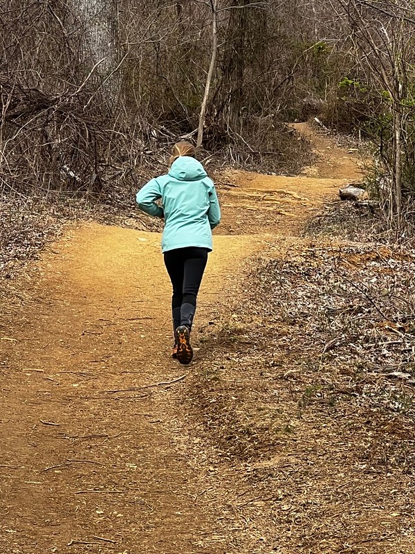 Woman running uphill on a trail in the woods.