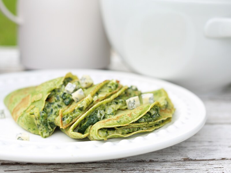 A white plate with folded, green pancakes on it.