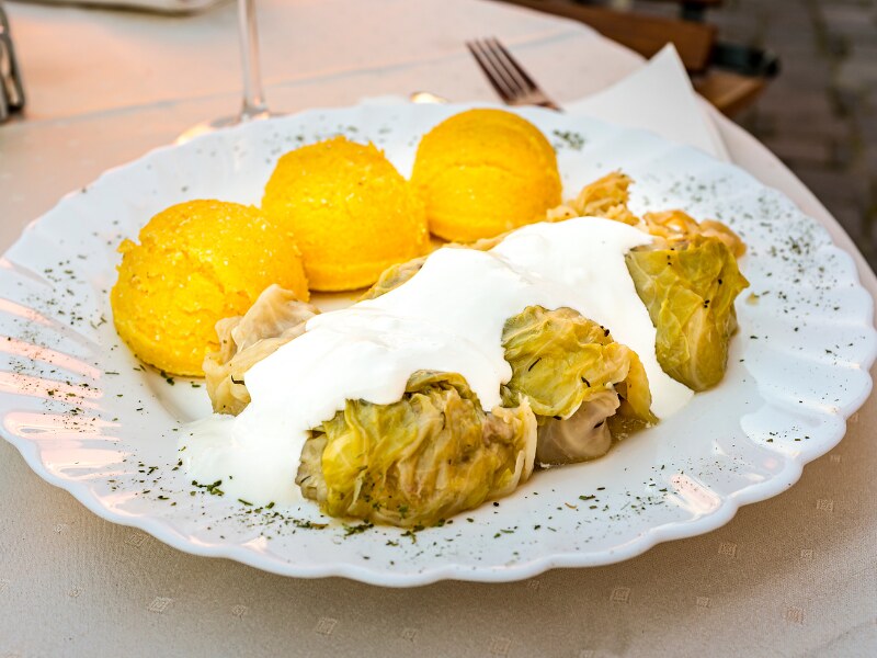 A white plate with three cabbage rolls on it, covered with sour cream. Besides them there are three dollops of polenta