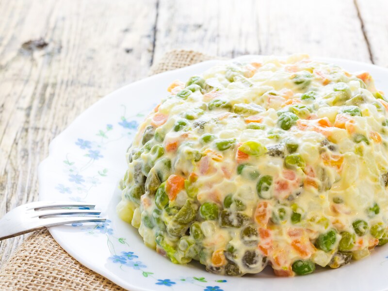 The a la Russe salad arranged in the shape of a dome. It is covered with mayo. You can see chopped carrots, potatoes, and peas in it.