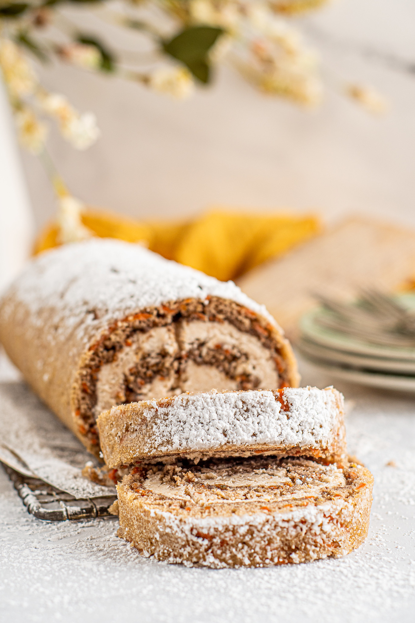 Carrot cake roll dusted with powdered sugar with 2 slices in the foreground