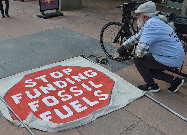 Demonstrator kneels next to banner at Chase Bank fossil fuel protest.