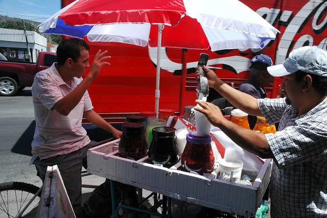 Hola! Preparing fruited ice, ice stand, jars of fruit, red, white, blue, umbrella, cart, Mexico