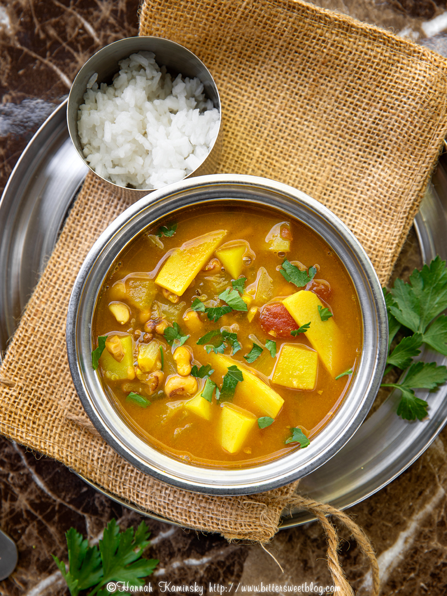 A metal bowl of black eyed pea curry soup with a side of white rice on a tray.