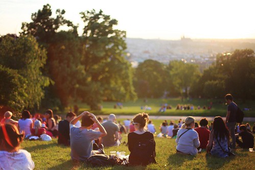 People sit on a grassy hill overlooking a city. 