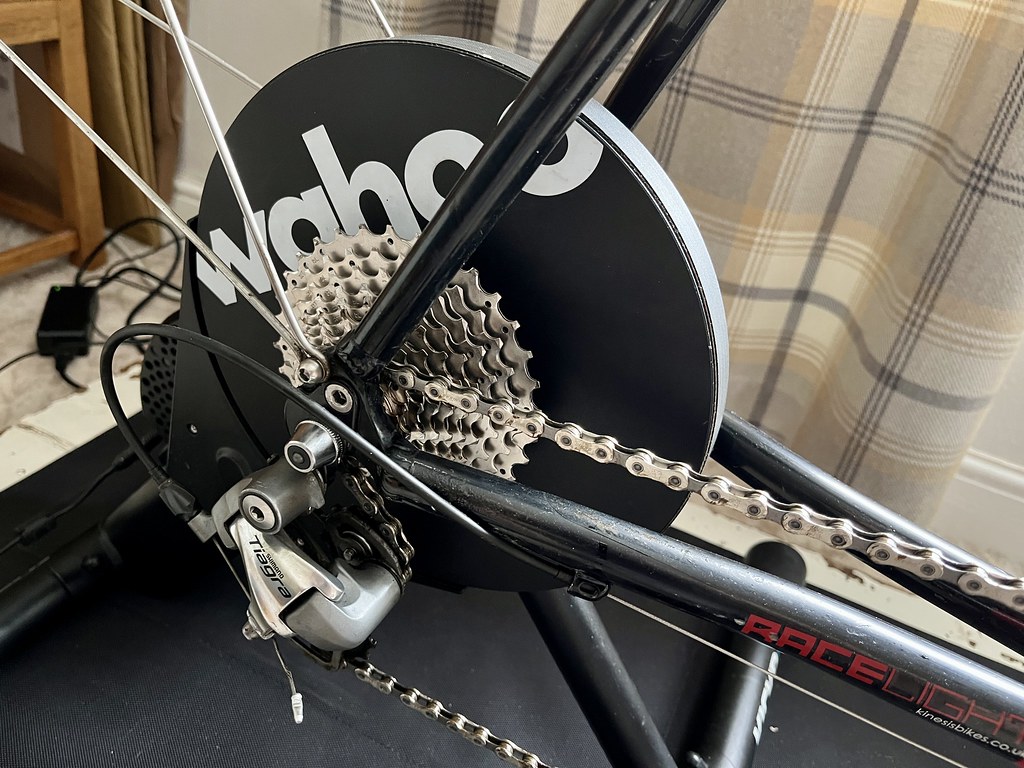 A photo of the Wahoo Kickr Core, a large black disk on legs, with 'wahoo' written across it in bold white letters. It's supporting the rear of a black-framed bike.