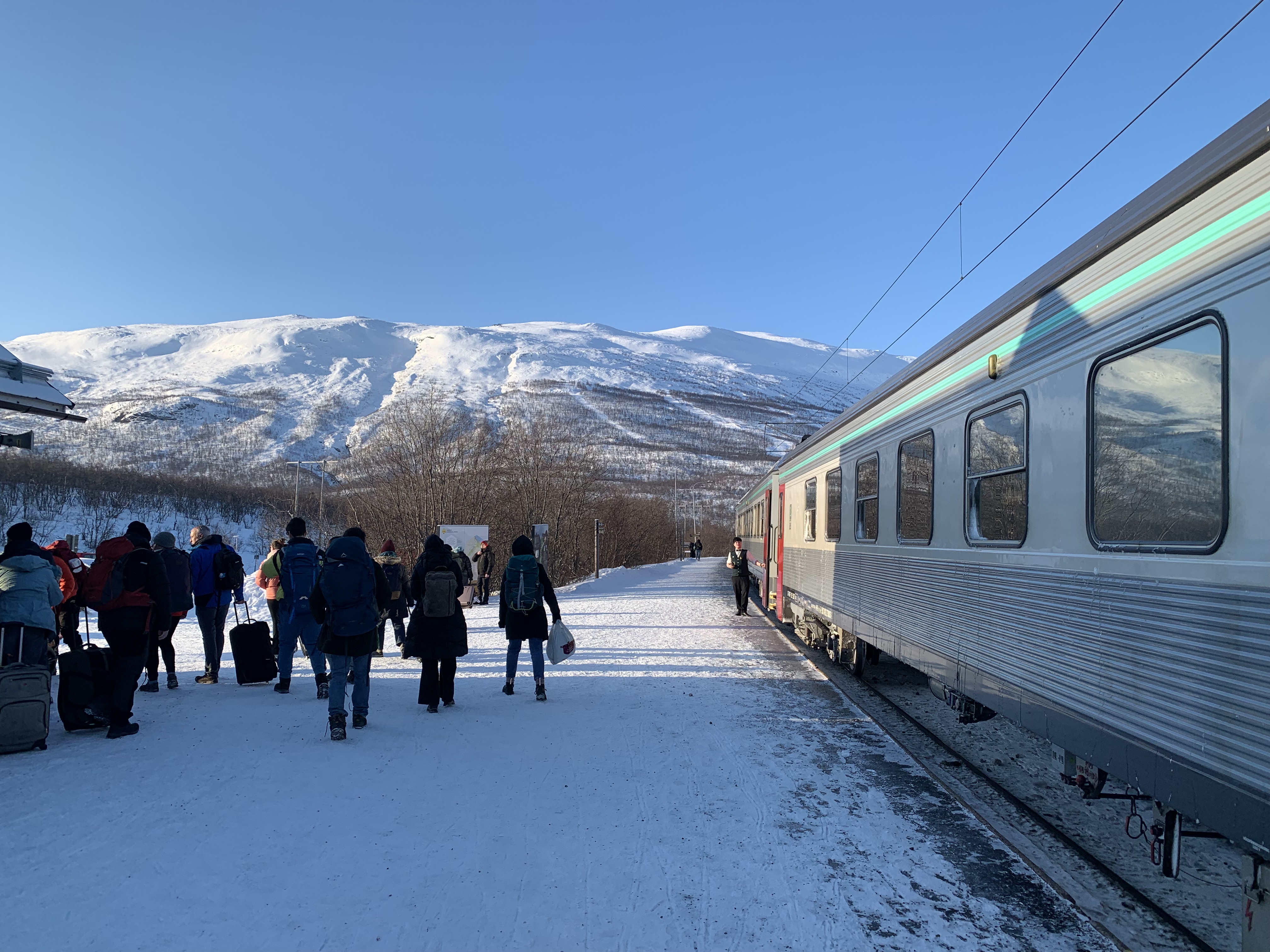 Le train en gare, montagne enneigée en arrière-plan, un groupe de gens part de la gare