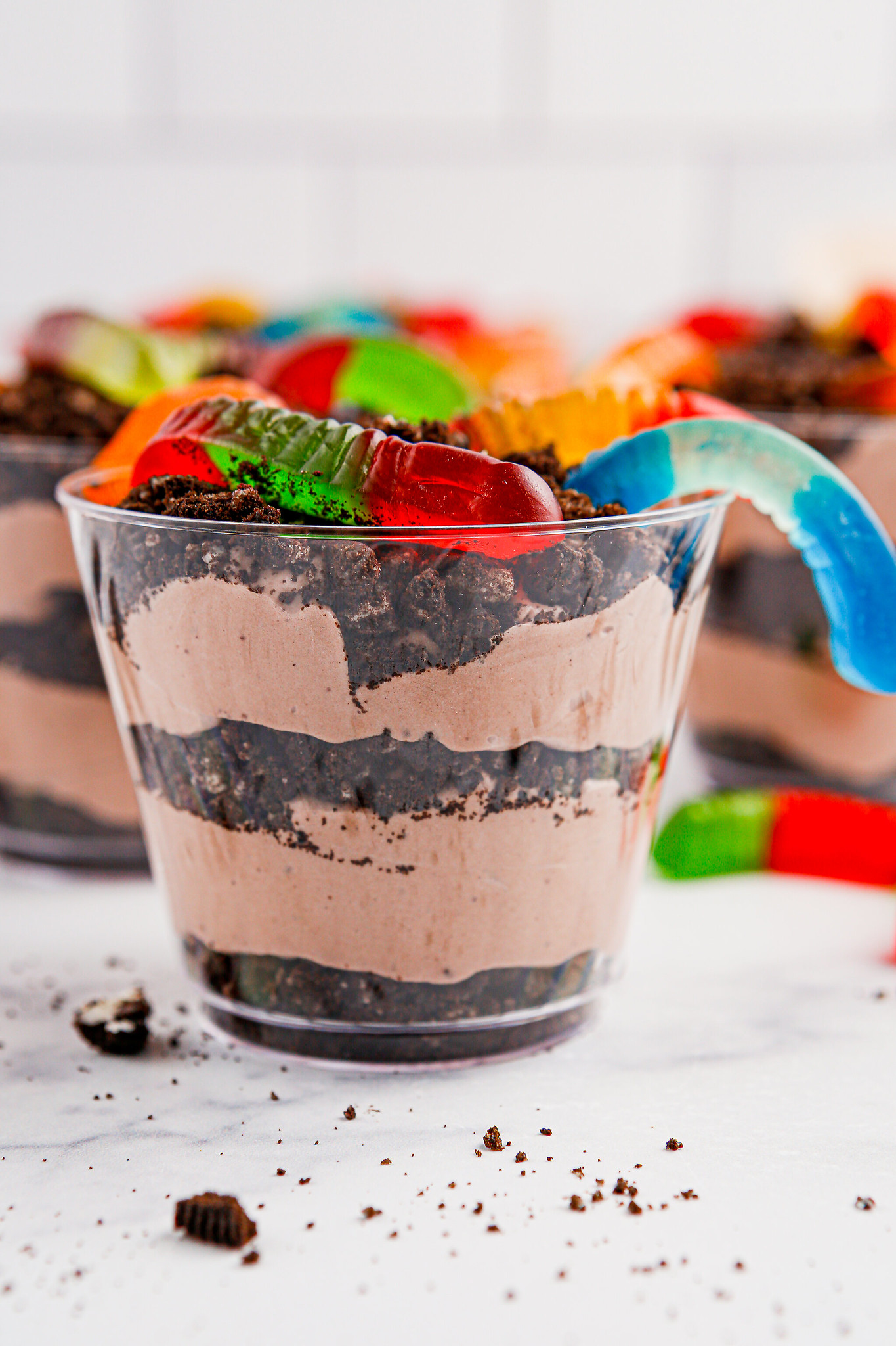 Individual cups of layered chocolate pudding and crushed Oreo cookies with gummy worms on top