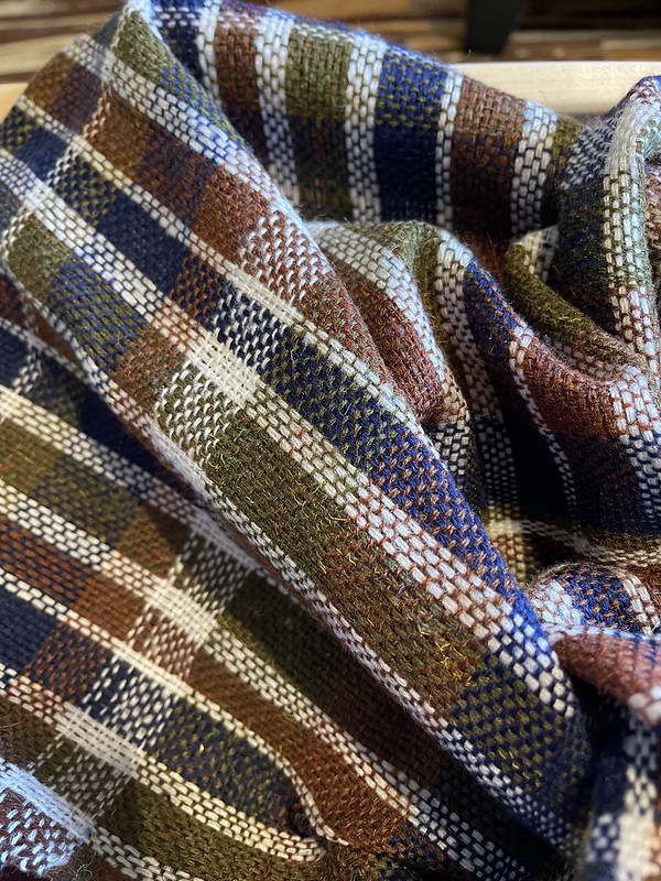 Folds of olive, dark red, blue, and white plaid fabric. The white looks prominently stripey, and there are larger bands of green and blue near the center of the shot