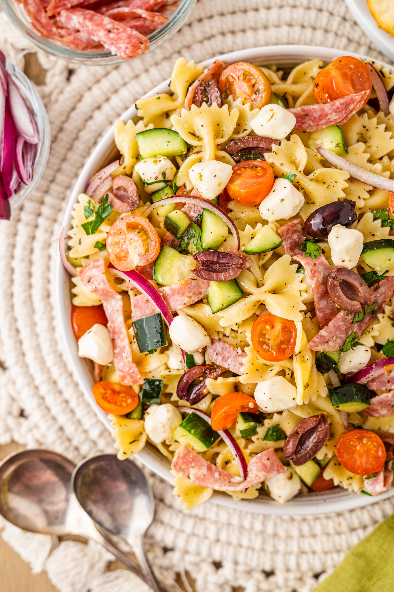 Overhead shot of pasta salad with sliced salami, mozzarella, diced cucumbers, cherry tomatoes, red onion, and parsley in an Italian dressing