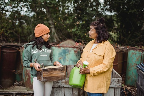 Two women stand in a garden. One holds a wooden box and one holds a green watering can - How to Talk to Your Family About Making Your College Decision