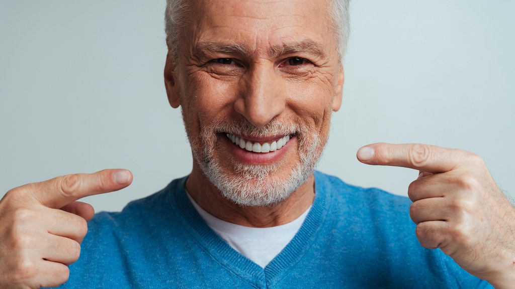 A photo of a middle-aged man pointing to his teeth while smiling