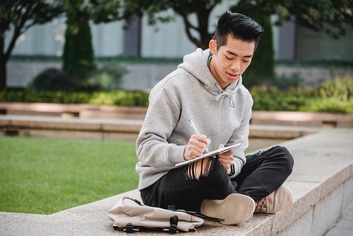 A man in a grey sweater and ripped jeans sits cross-legged and writes in a notebook - How to Change Your Major in College