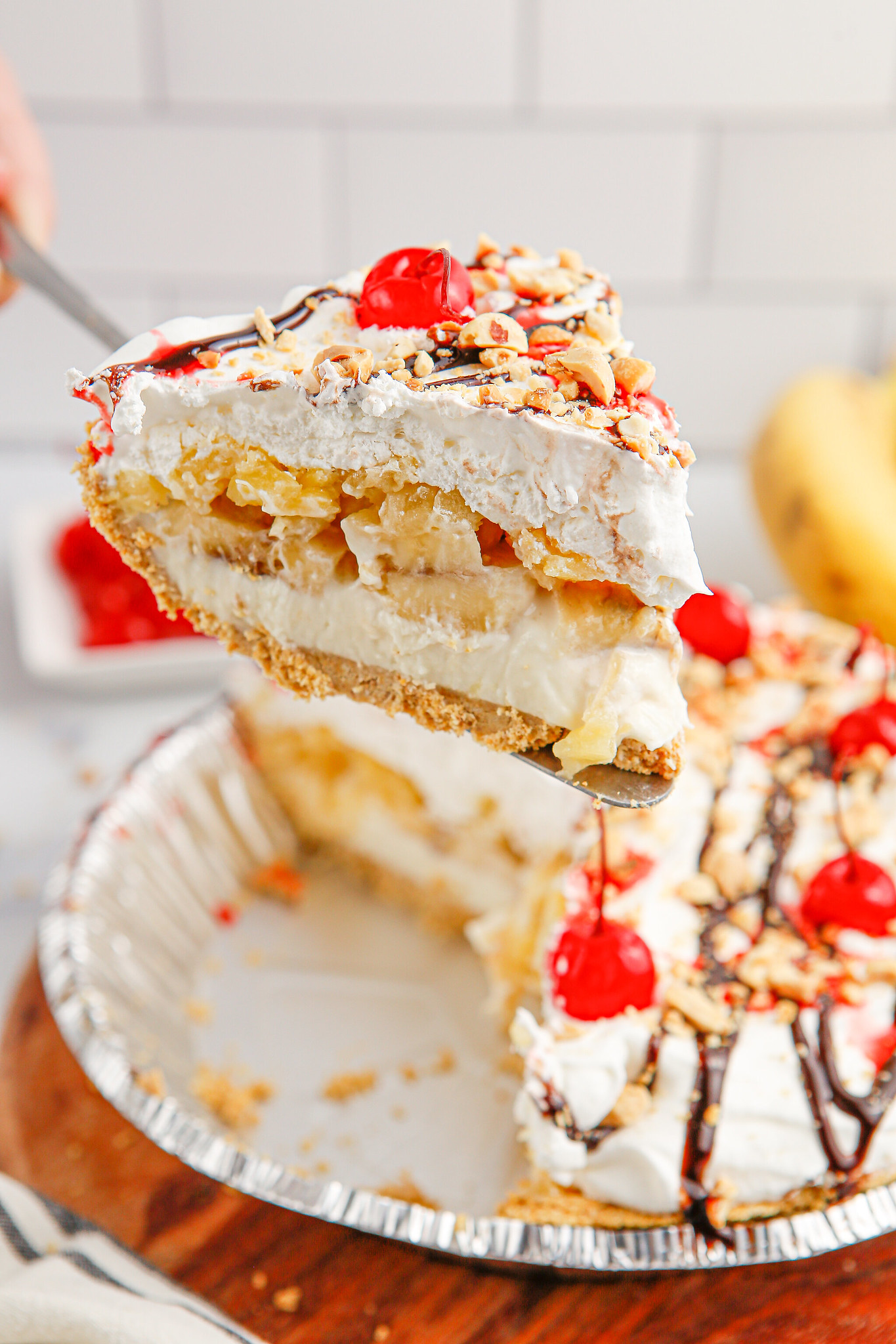 A slice of banana split pie being lifted out of the pie plate with the rest of the pie behind it