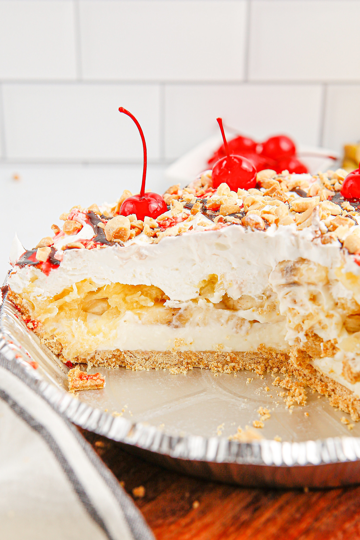 Cross section of banana split pie with layers of graham cracker crust, bananas, pineapple, and whipped cream