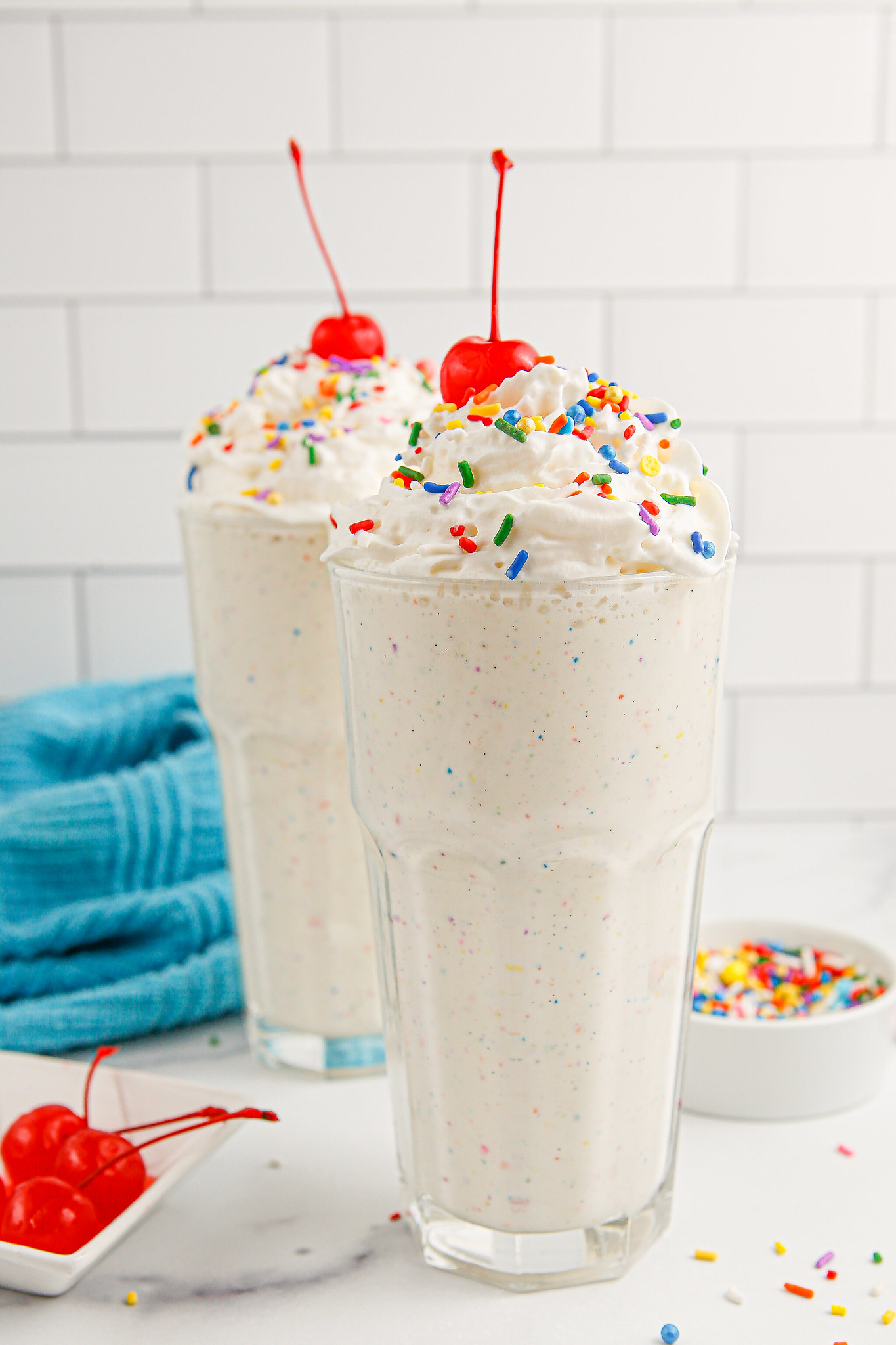 Cake Batter Milkshakes topped with whipped cream, rainbow sprinkles, and a cherry