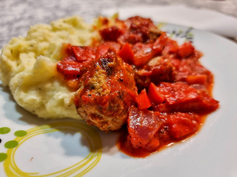 A close-up of the meatballs on the plate, covered with the red sauce, next to the mashed potatoes.