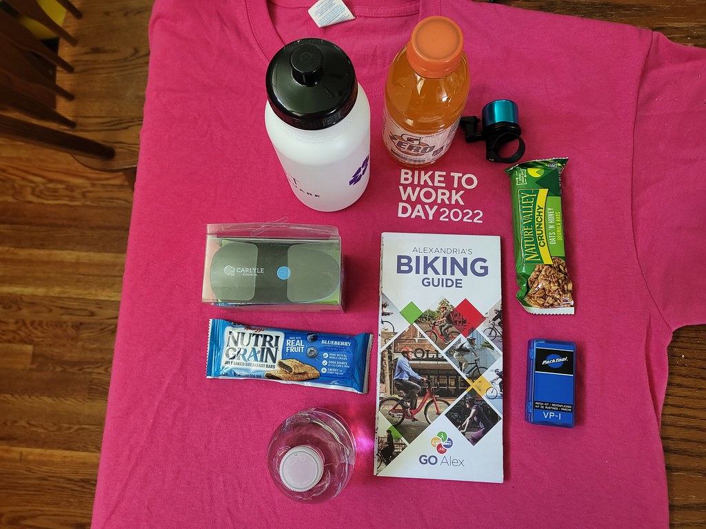 2022 Bike to Work Day swag, including a water botle, granola bar, bike bell, map, Nutri Grain bar and pink t-shirt.