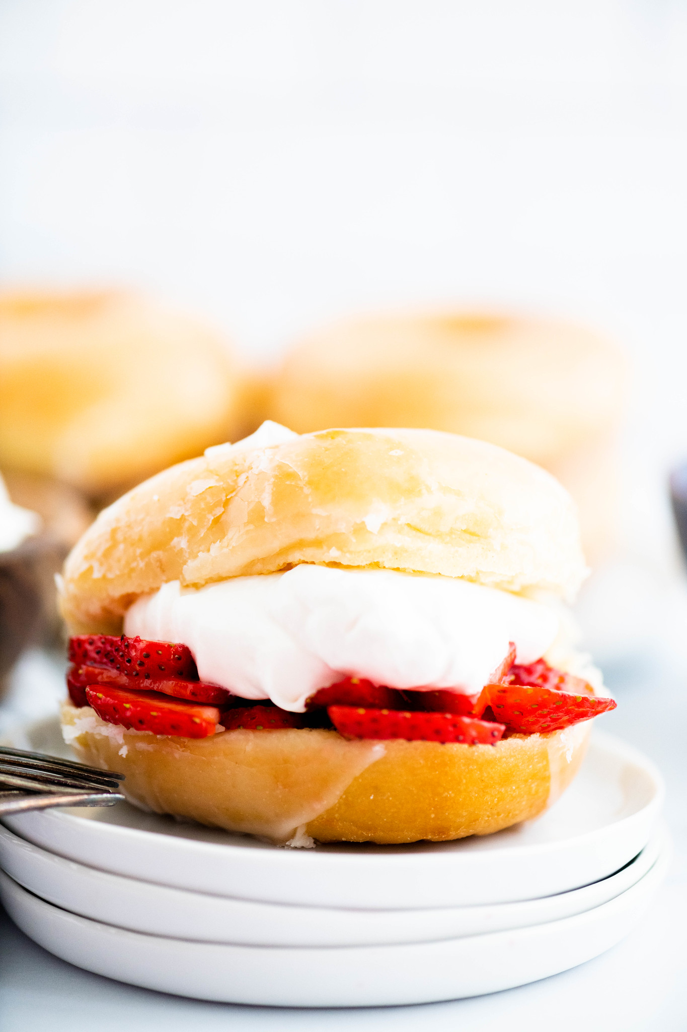 Close up of glazed donut filled with sliced, macerated strawberries and fresh whipped cream.