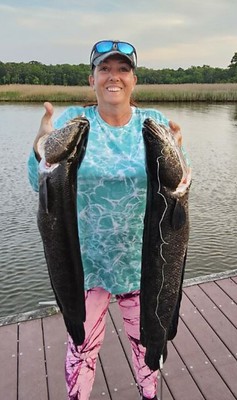 Photo of woman on a dock holding two large snakehead fish