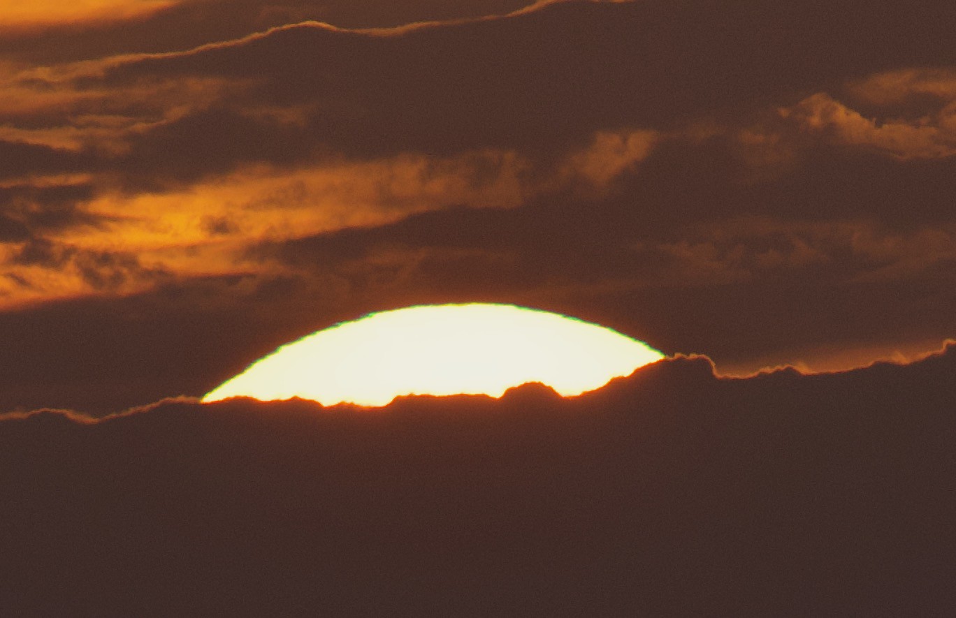 Green Flash on the setting Sun over the ocean & through clouds