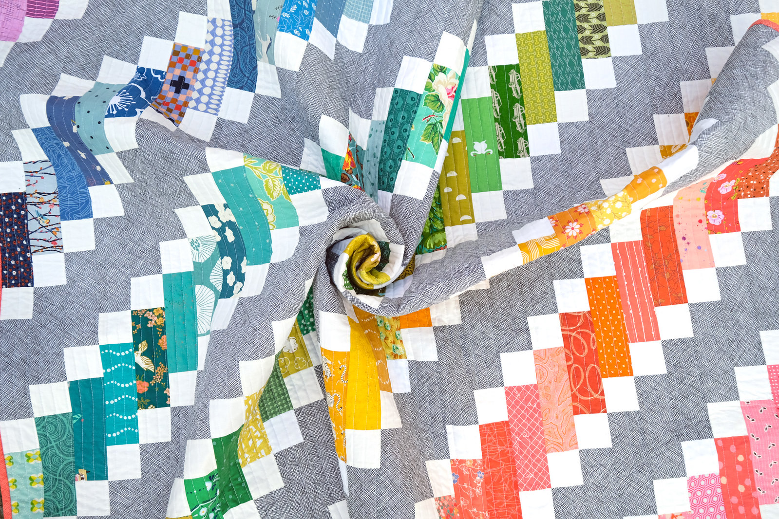 A vibrant rainbow quilt using the Ruby Quilt Pattern by Kitchen Table Quilting. The quilt is beautifully crafted with a rainbow of colorful scraps, creating a stunning visual display of patchwork