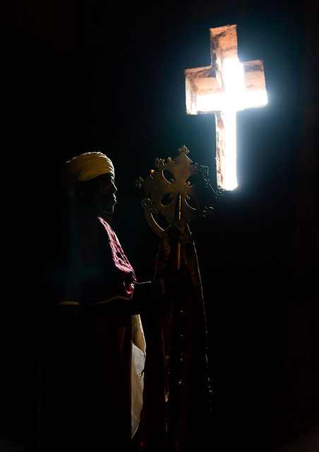 Ethiopian orthodox priest holding a cross inside a rock-hewn church, Amhara Region, Lalibela, Ethiopia