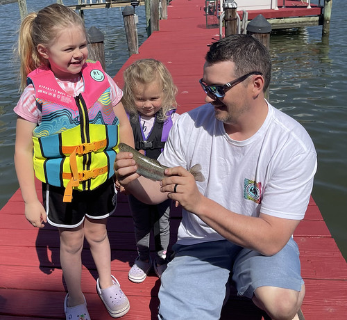 Photo of man with two young daughters on a pier, holding a fish